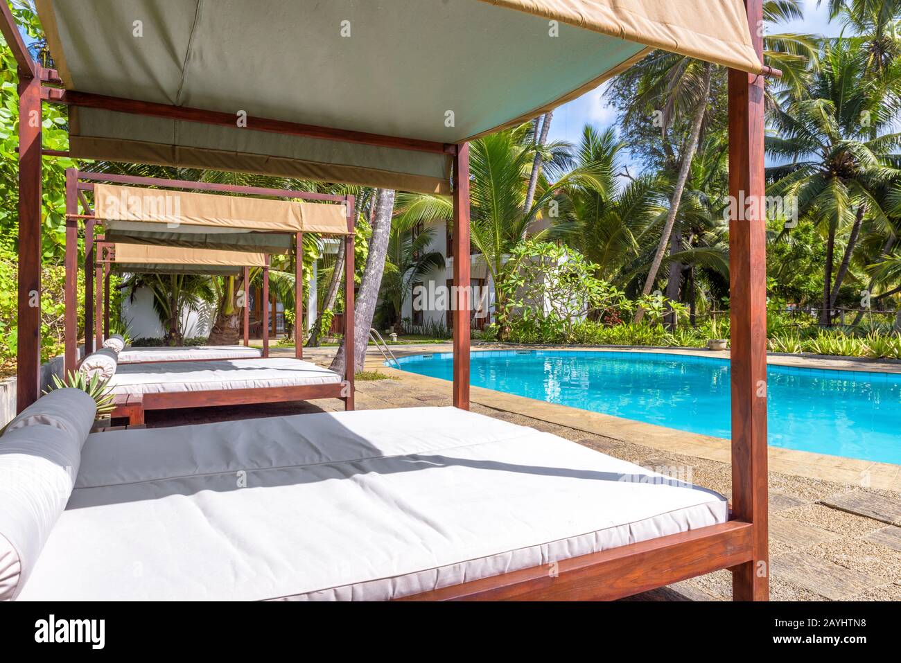 Tangalle, Sri Lanka - November 4, 2017: Beach beds in a tropical hotel. Swimming pool with blue water in tropics. Beautiful idyllic resort among palm Stock Photo