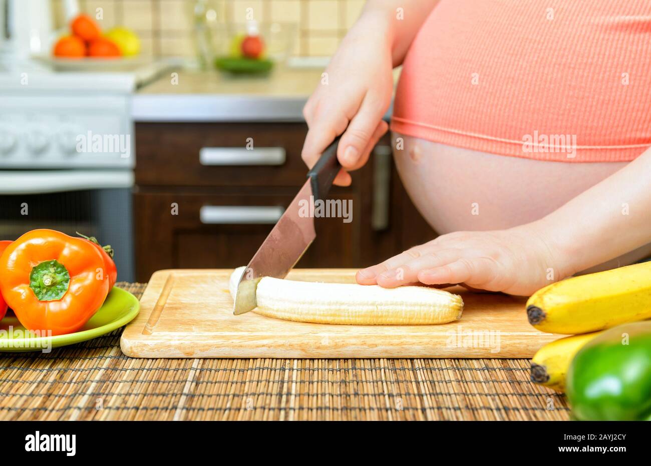 Pregnant woman prepares a banana in the kitchen. Healthy food Stock