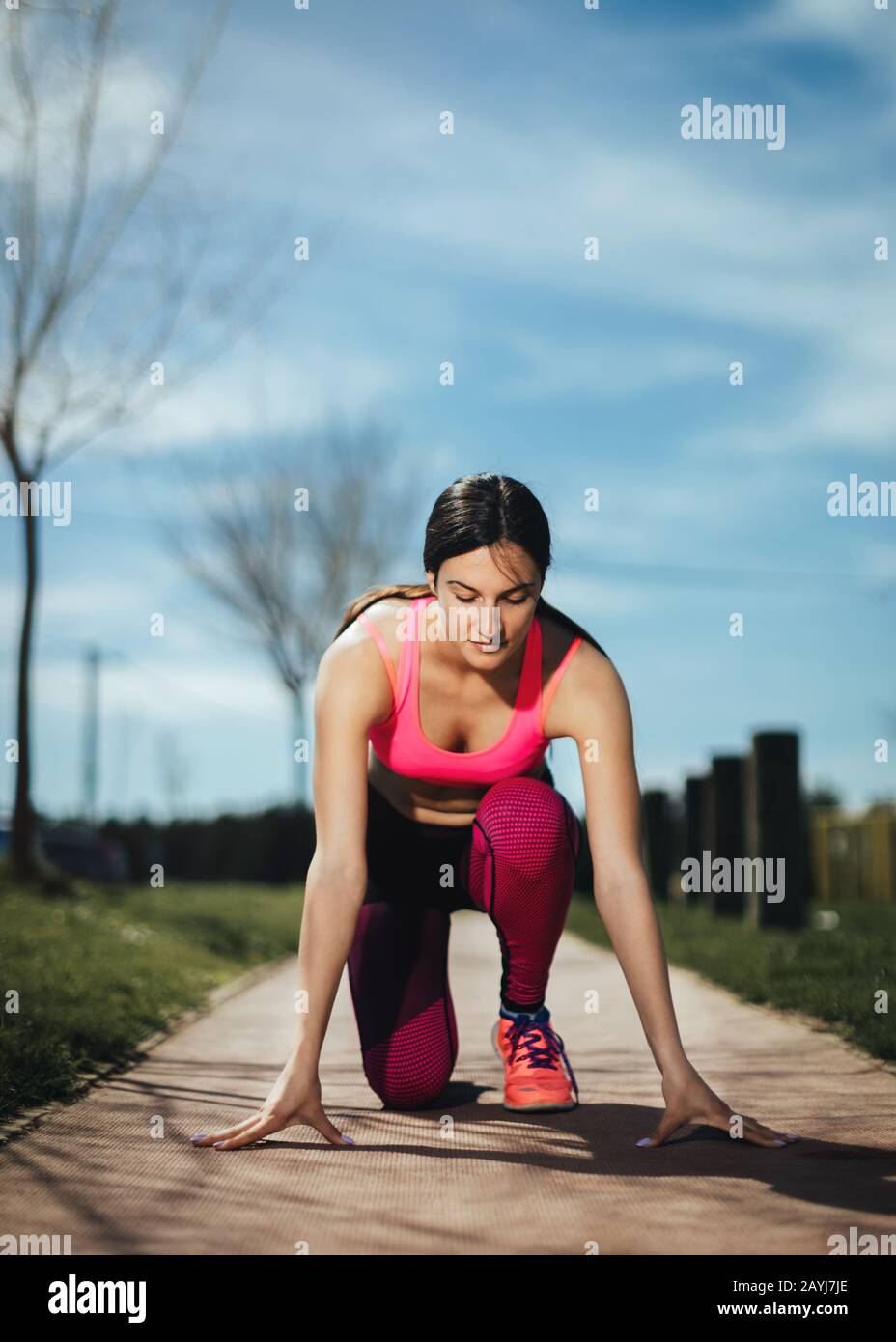 Young athlete woman preparing to start running. Female jogger in start position on the track in park. Healthy recreation concept. Stock Photo