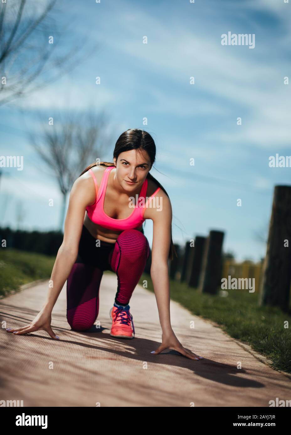 Young athlete woman preparing to start running. Female jogger in start position on the track in park. Healthy recreation concept. Stock Photo