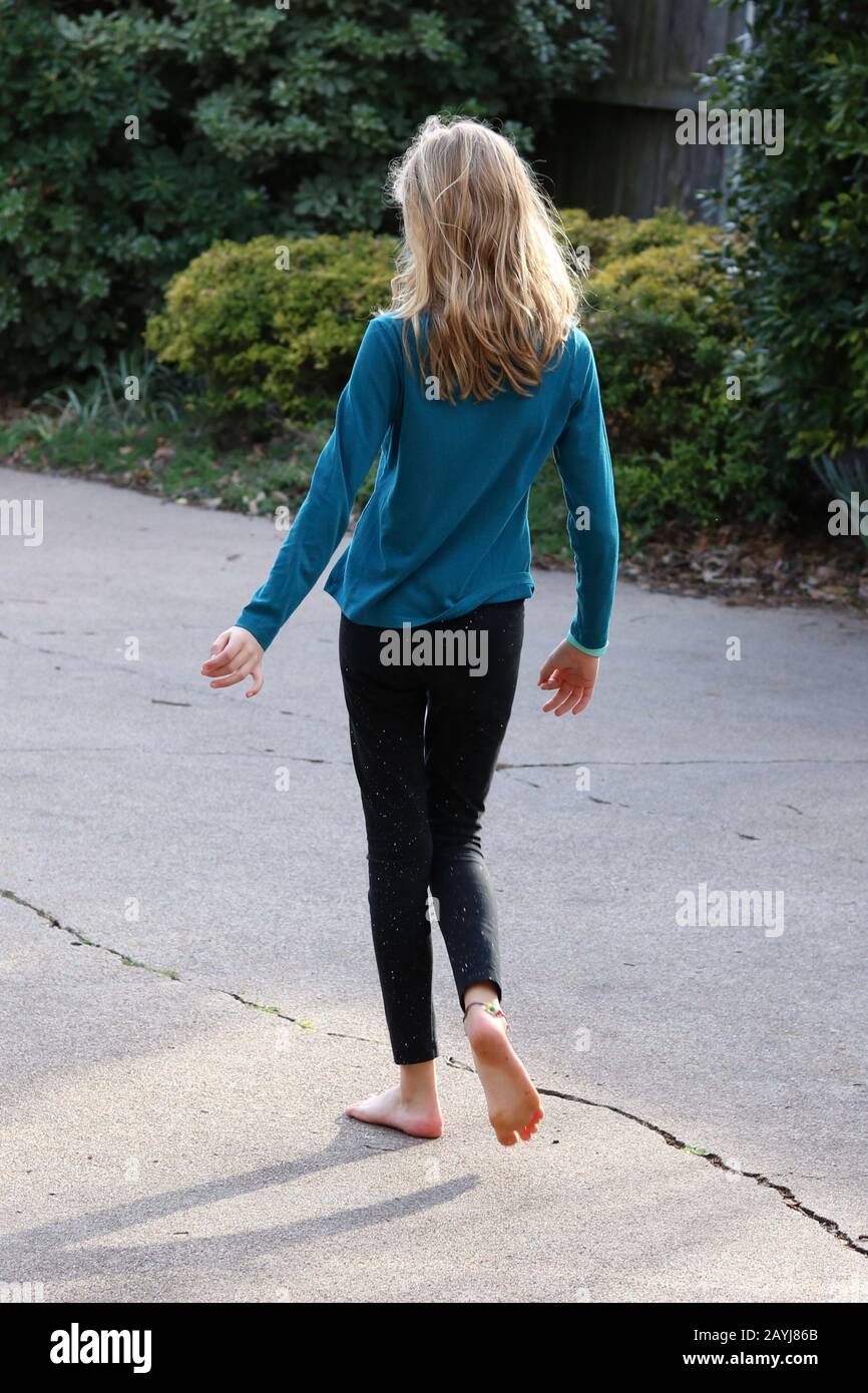Girl with long blonde hair and on bare feet seen from behind as she is walking away wearing casual clothes Stock Photo