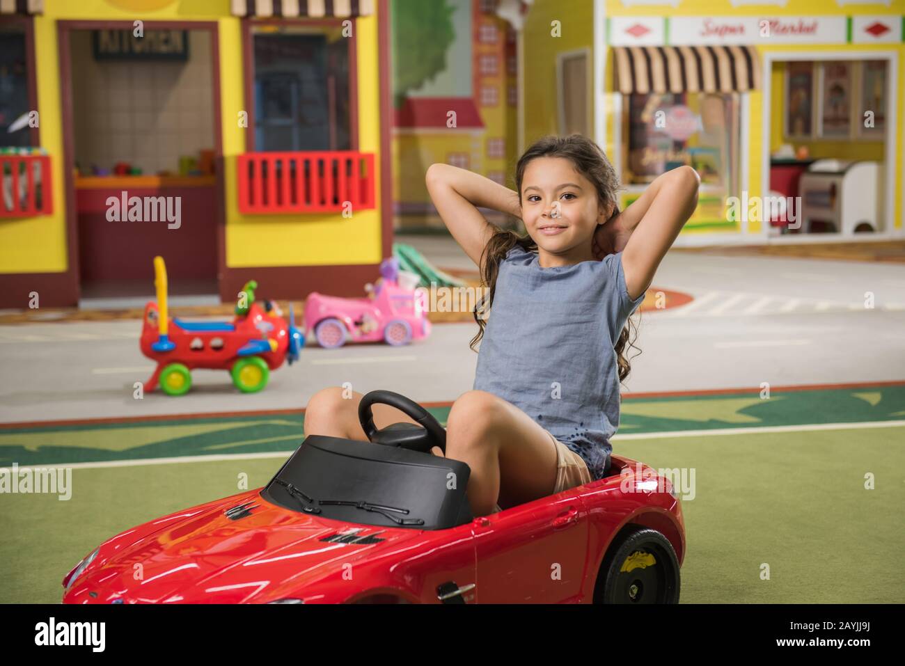 Happy little girl sitting in toy car at indoor playground Stock Photo ...