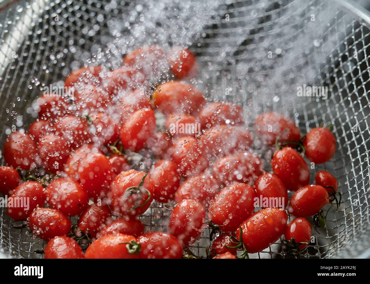 Cleaning the vivid red ripe tomatoes in the metal wire basket Stock Photo