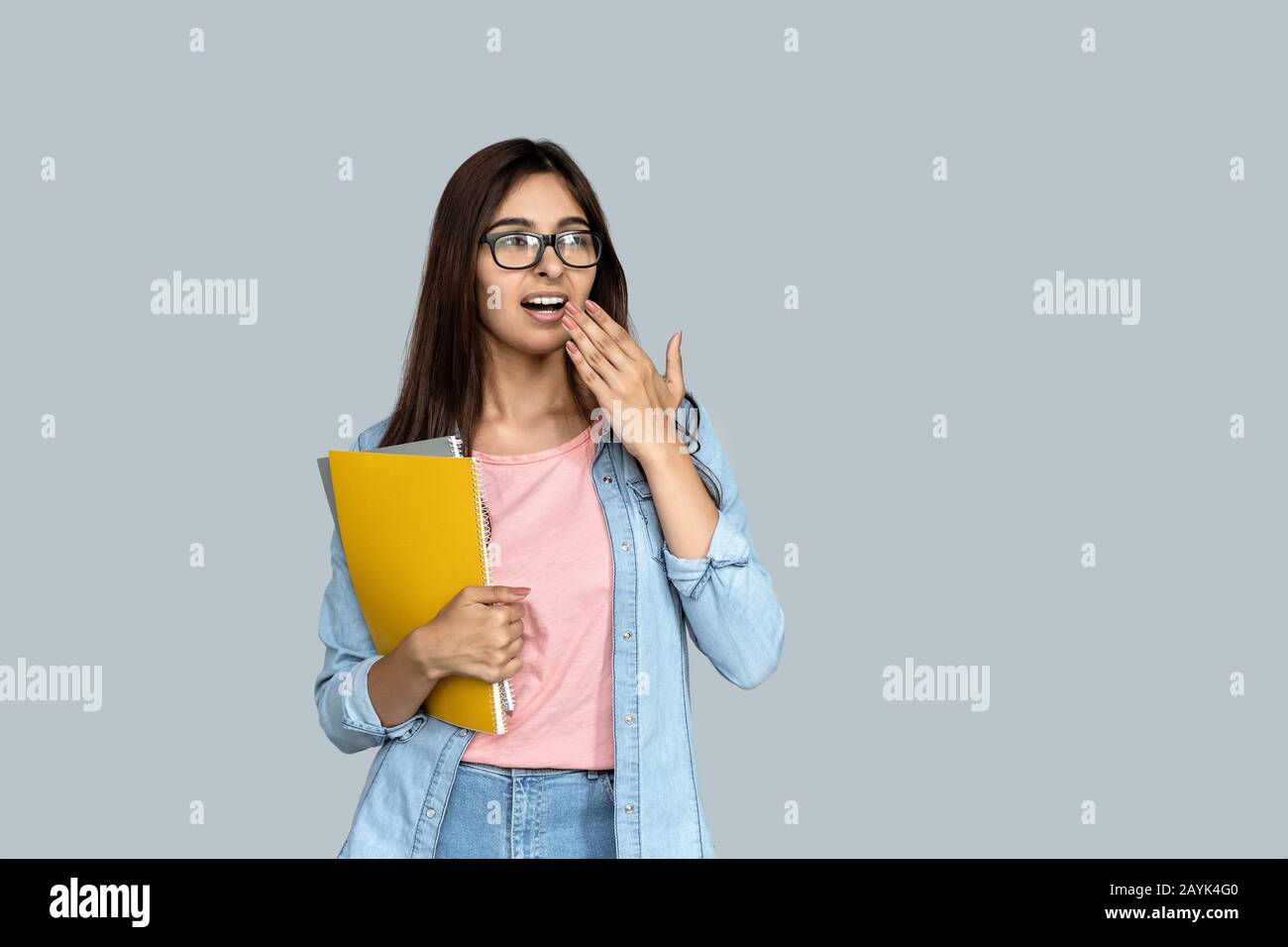 Bored adult indian student girl with copybooks covering mouth with hand Stock Photo