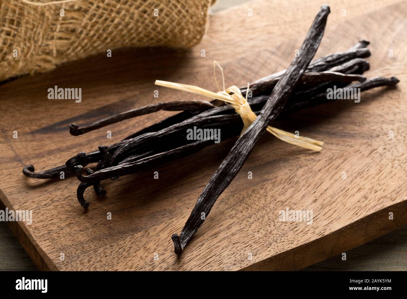 Bundle of tied, dried bourbon vanilla beans or pods on brown wooden cutting board with burlap sack - selective focus Stock Photo