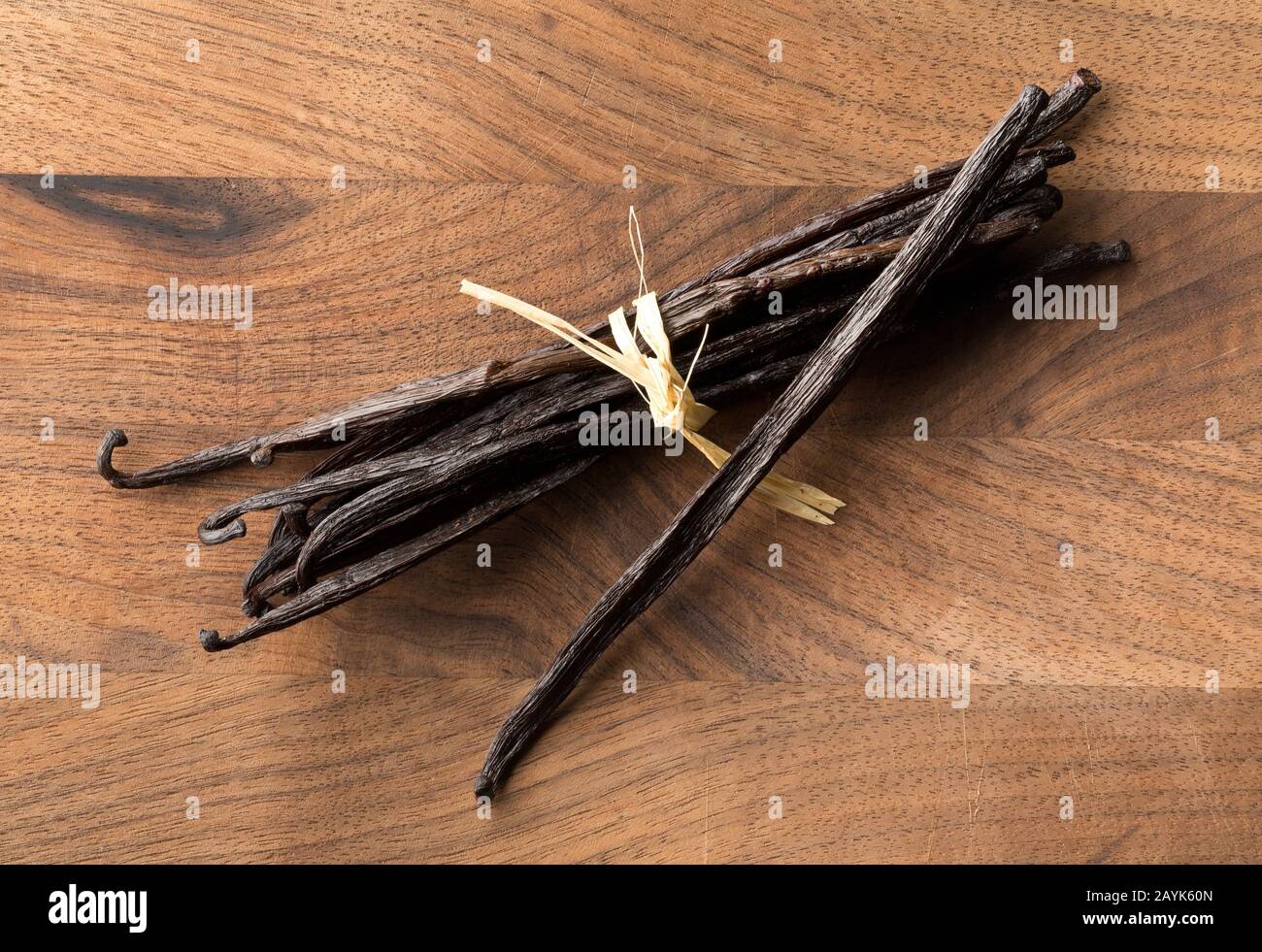 Bundle of tied, dried bourbon vanilla beans or pods on brown wooden cutting board flat lay top view from above Stock Photo
