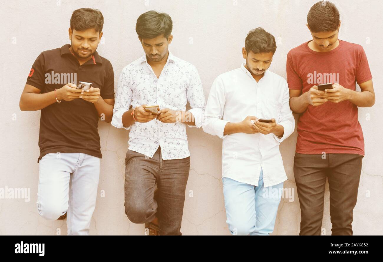 Young people with heads down busy on smart phone - Friends group using smartphone againt wall at backyard - Concept of millennials addicted and Stock Photo