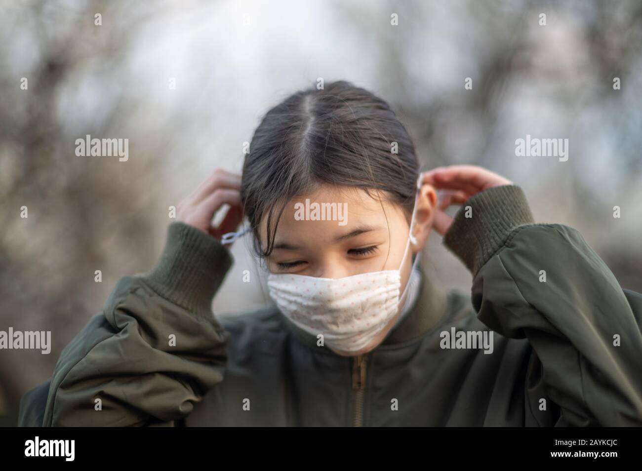 Young girl /child of mixed Asian -European ethnicity putting on a face mask to avoid virus / allergy. Close up outdoor shot during Covid-19. Stock Photo