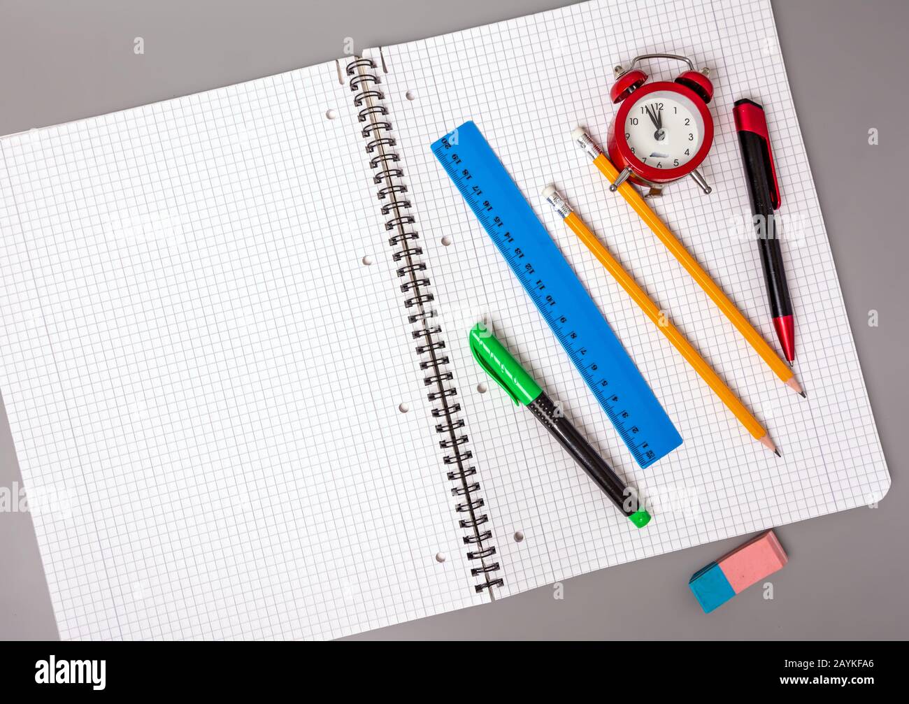 Pencils, a pen and a ruler lie on an open notebook. An alarm clock reminds of time. Office. School supplies. Stock Photo