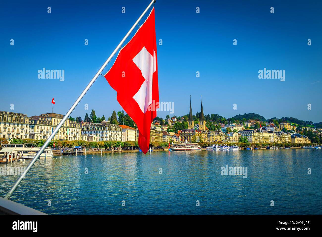 Popular travel place in Lucerne with famous buildings and Reuss river. Waving Swiss flag on the bridge with cityscape and river, Lucerne, Switzerland, Stock Photo