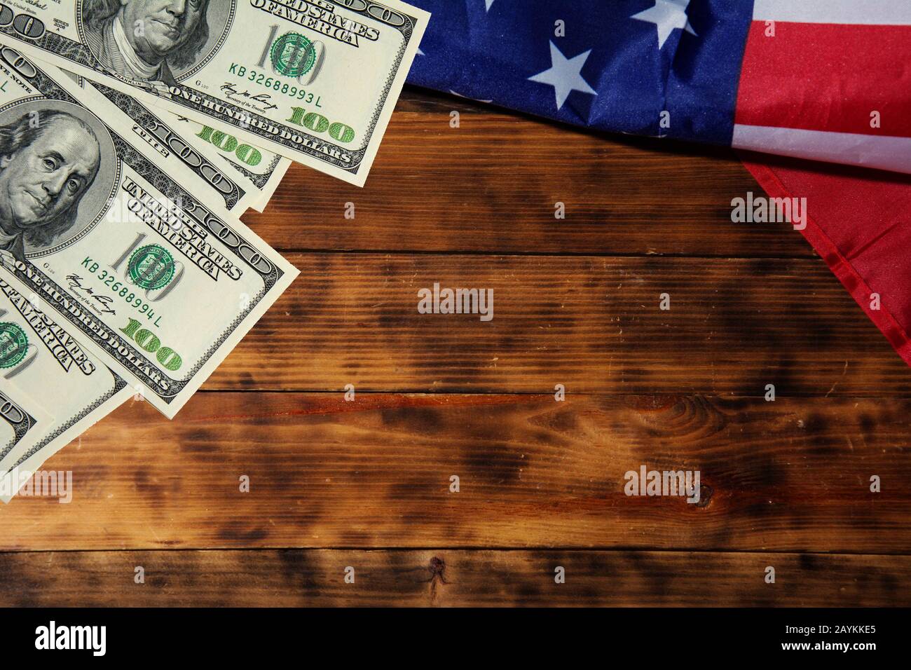 American flag and one hundred US dollar banknotes on old dark wooden background. Copyspace for text Stock Photo