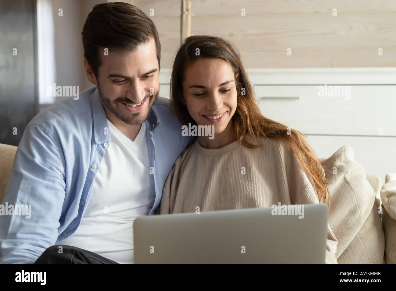 Smiling millennial couple relax on couch using laptop Stock Photo