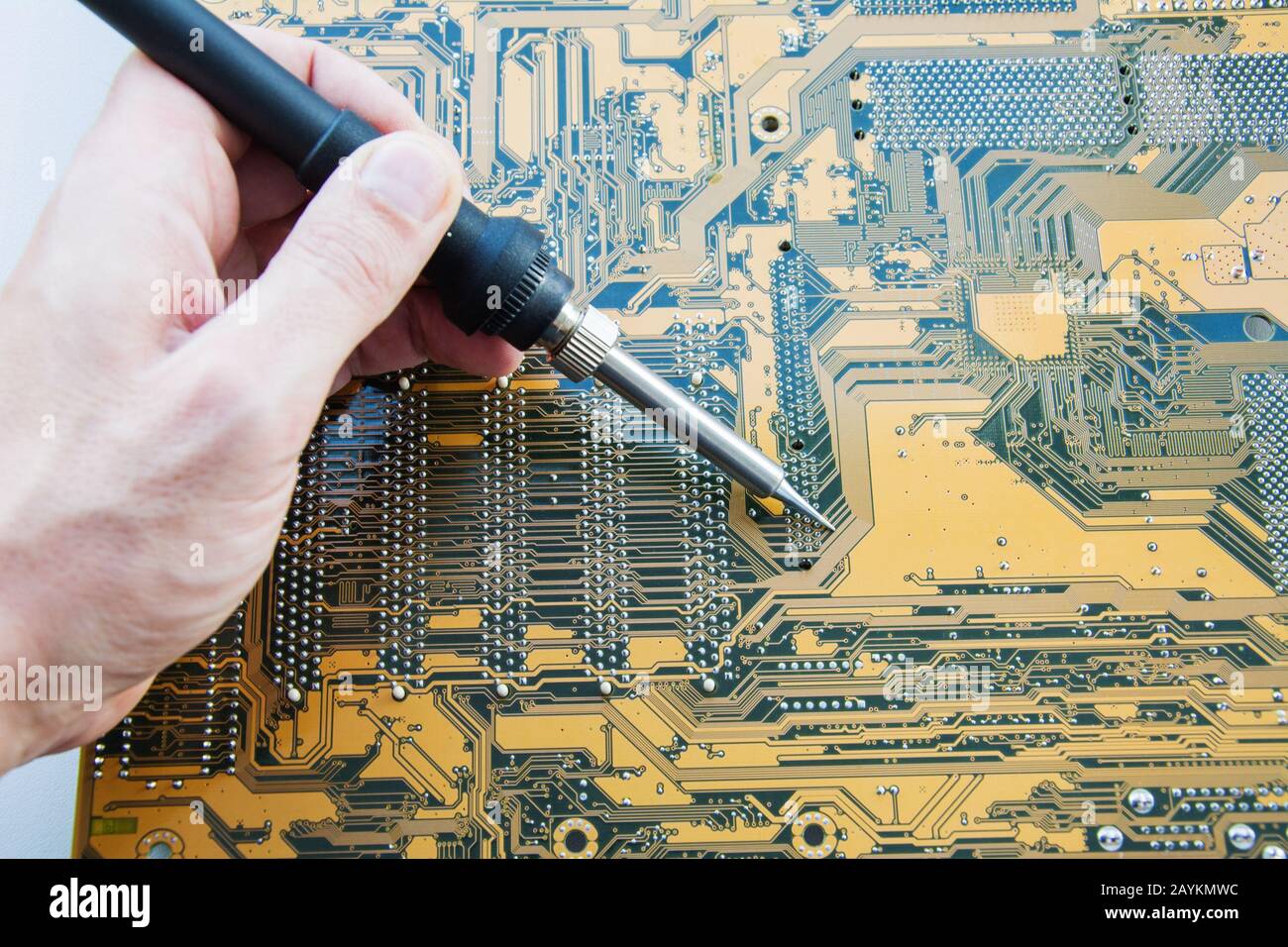 Service engineer electronics using a soldering iron performs repair of printed circuit of computer equipment. Electronics repair and tuning concept. Stock Photo