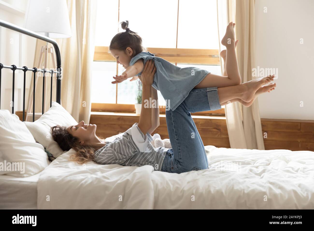 Happy young mother lifting little preschool child daughter in bedroom. Stock Photo