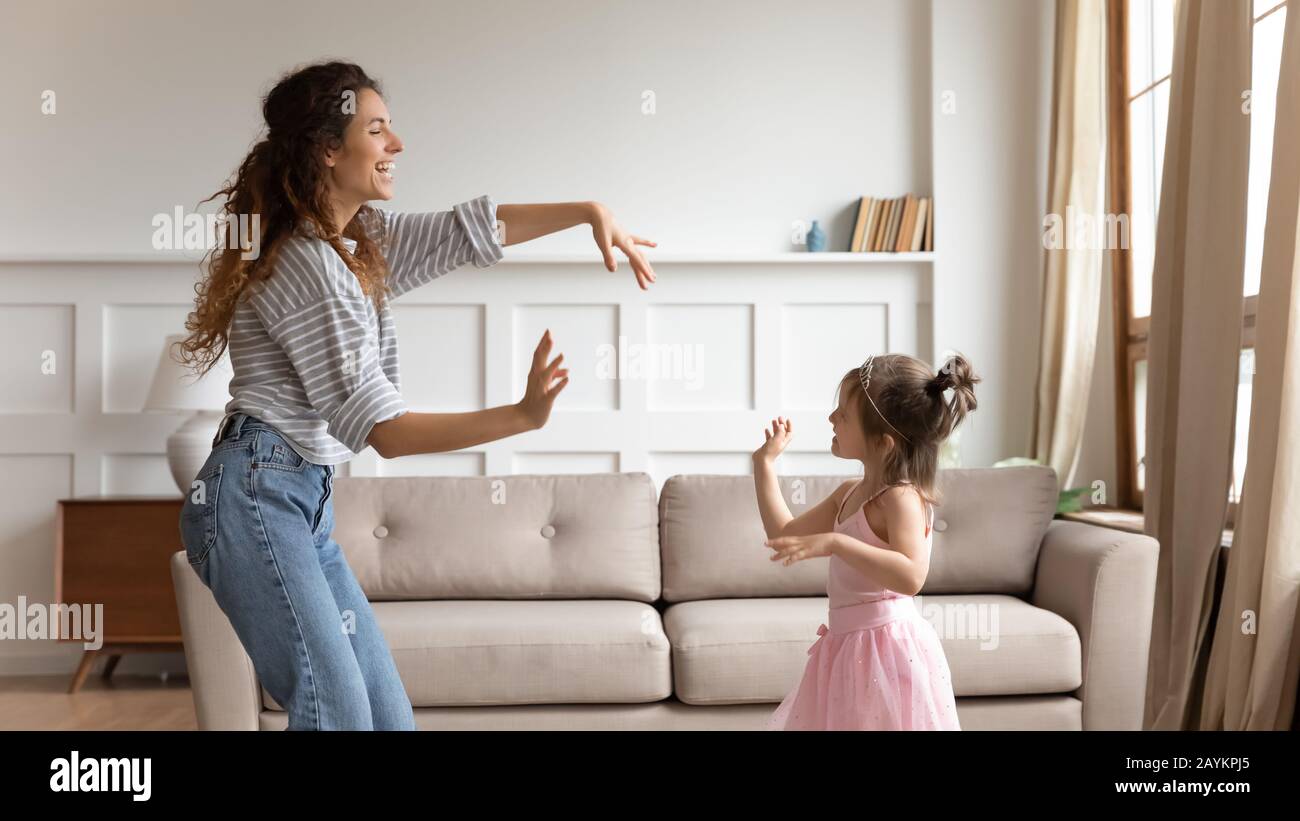 Young babysitter dancing to music with daughter at home. Stock Photo