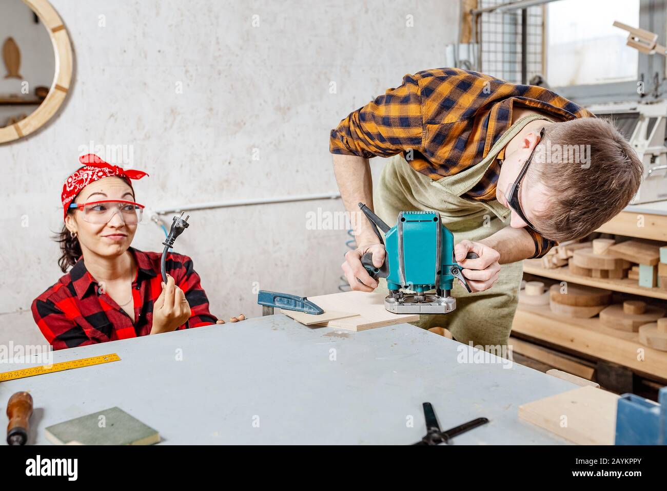 Male carpenter working with electric jigsaw and his girlfriend shows the plug socket. The concept of safety and humor Stock Photo