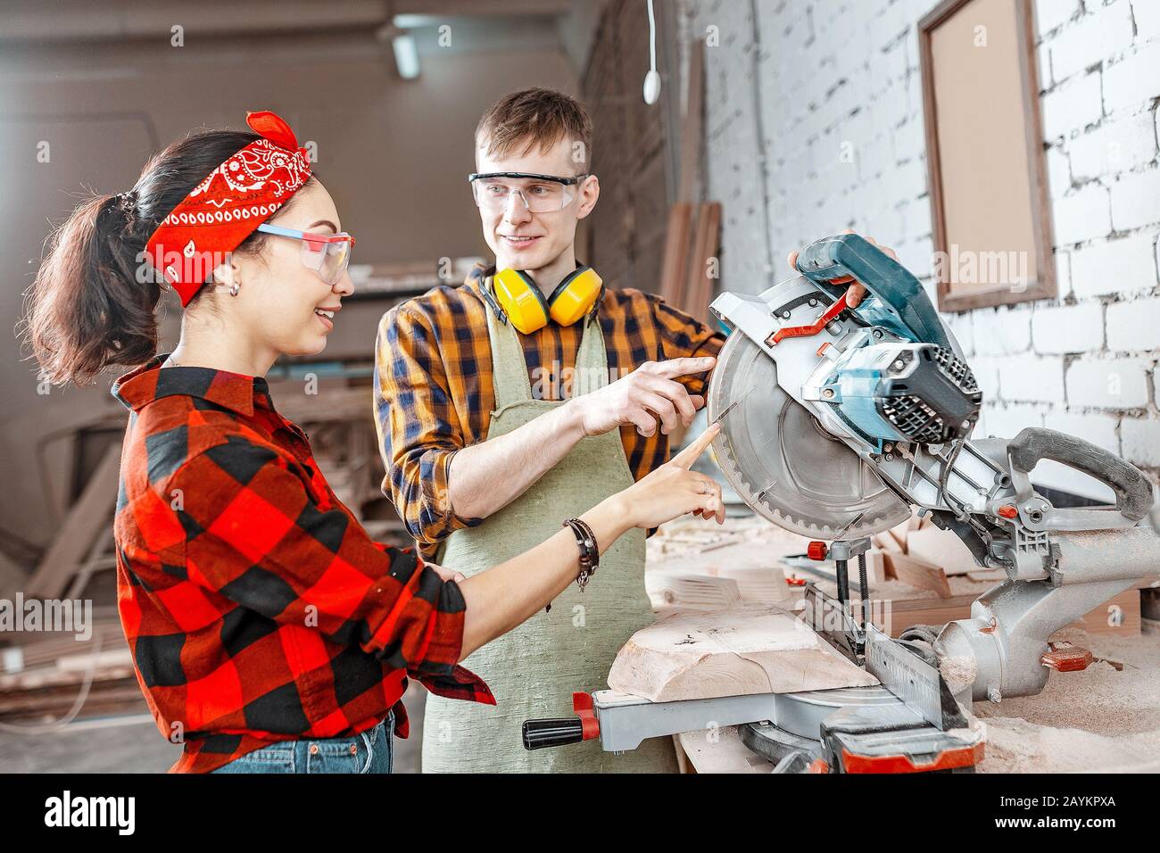 A male craftsman explains to a girl apprentice how to work with an automated saw machine in a factory or workshop Stock Photo