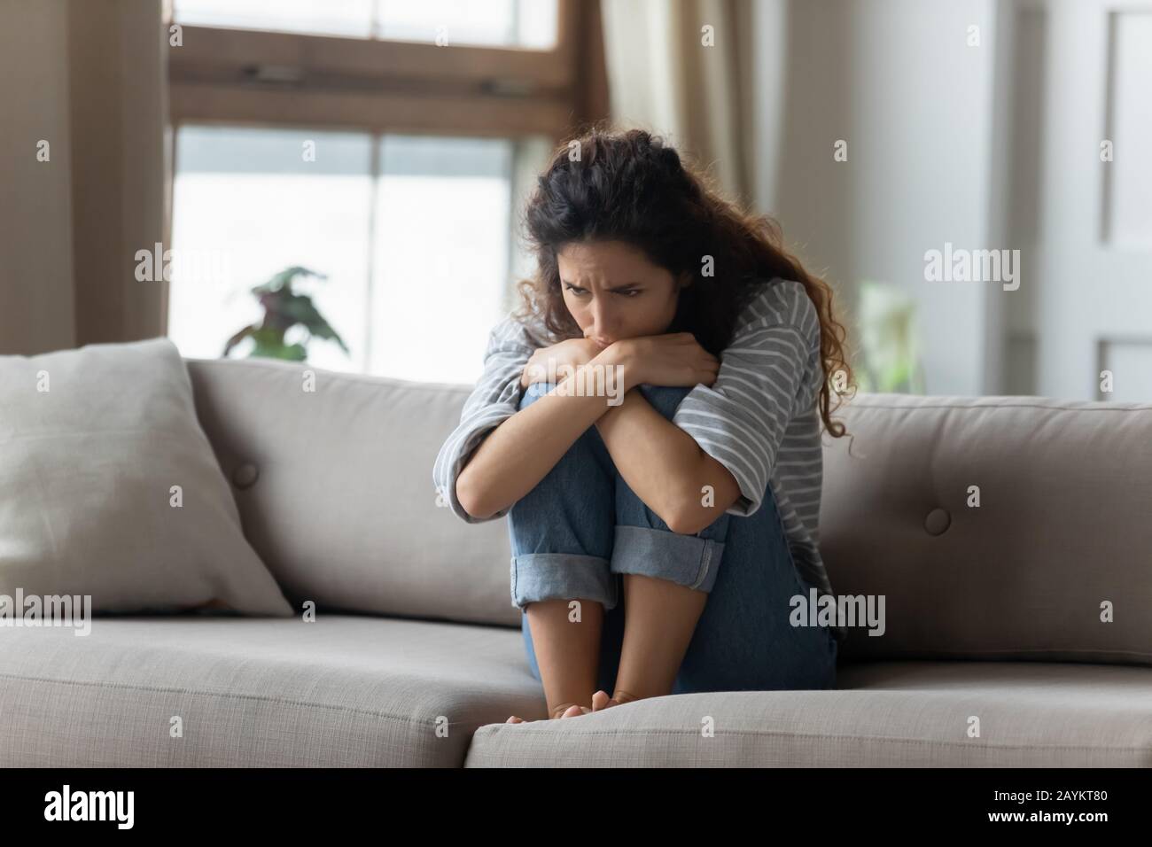 Stressed young woman embracing knees, sitting alone on couch. Stock Photo