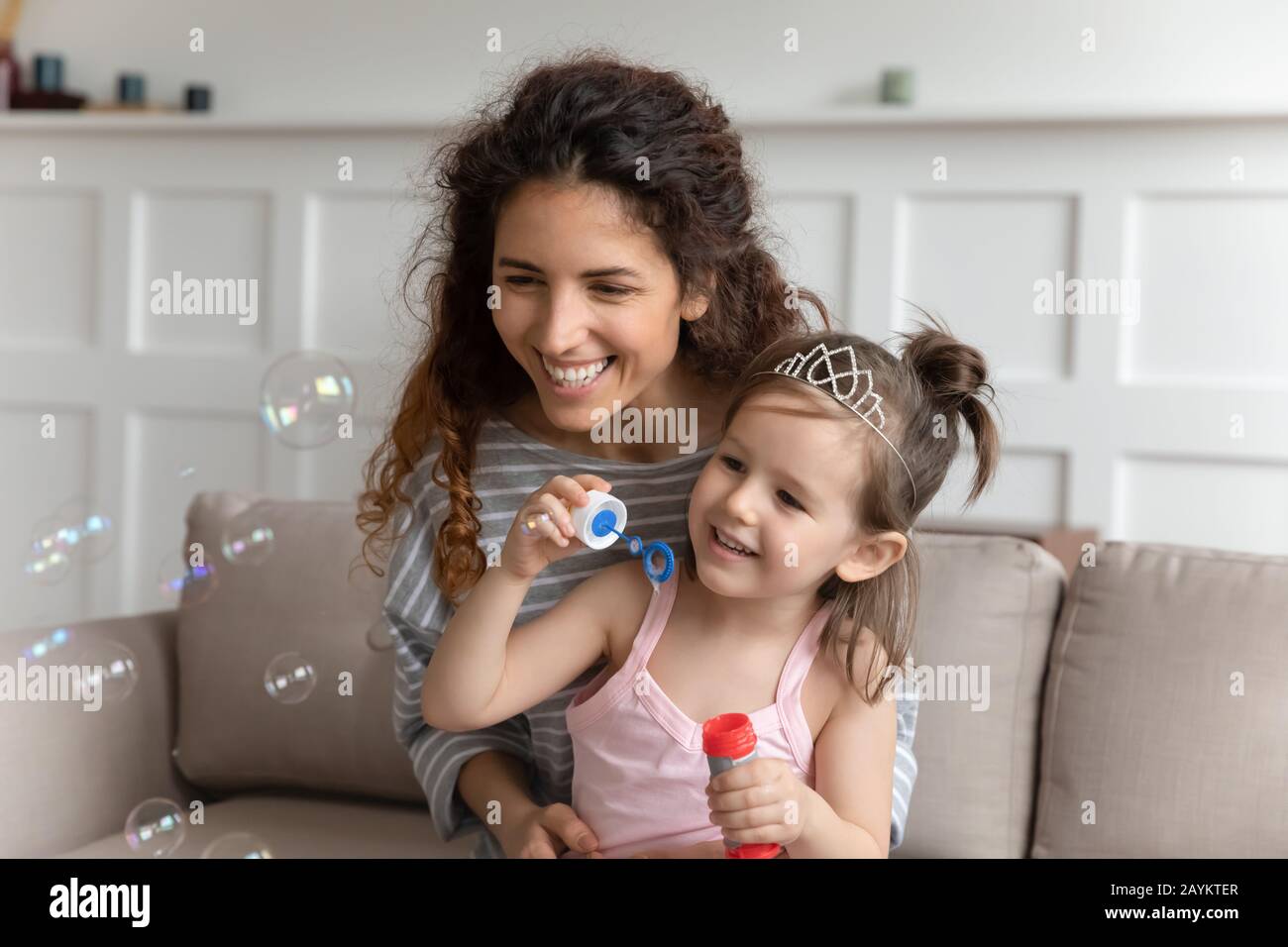 Pleasant young babysitter blowing soap bubbles with daughter. Stock Photo