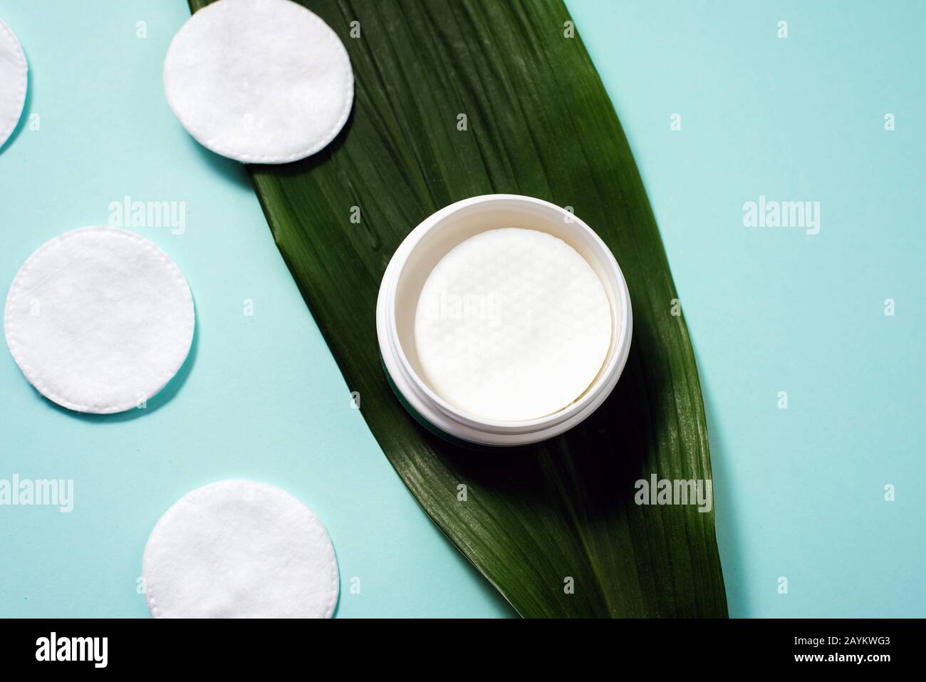Jar with cotton pads in liquid for cleansing the skin on a palm leaf. Cleaning cotton pads on a