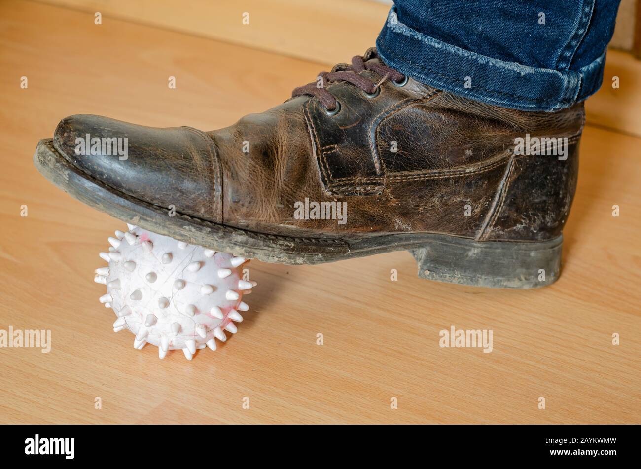A light rubber ball with spikes is pressed to the wooden floor with a dirty boot. Close-up. Selective focus. Stock Photo