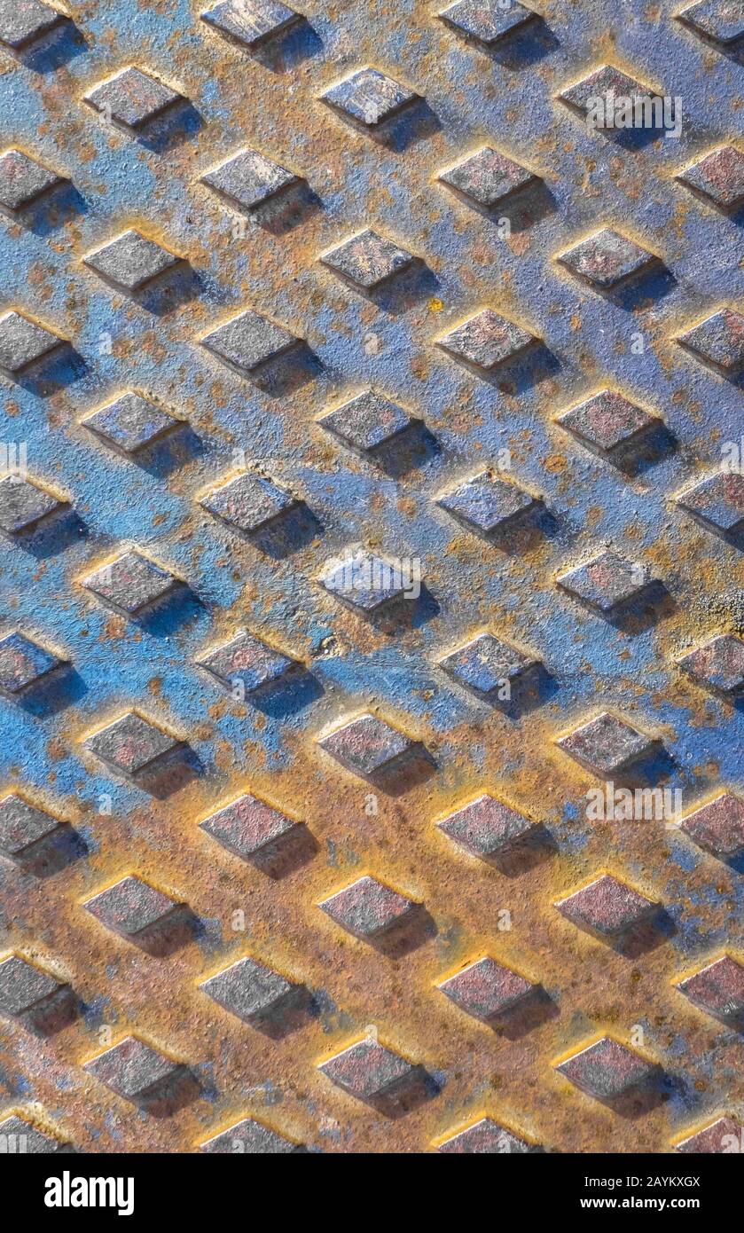 Old rusty drain cover background with diamond pattern. Orange and blue