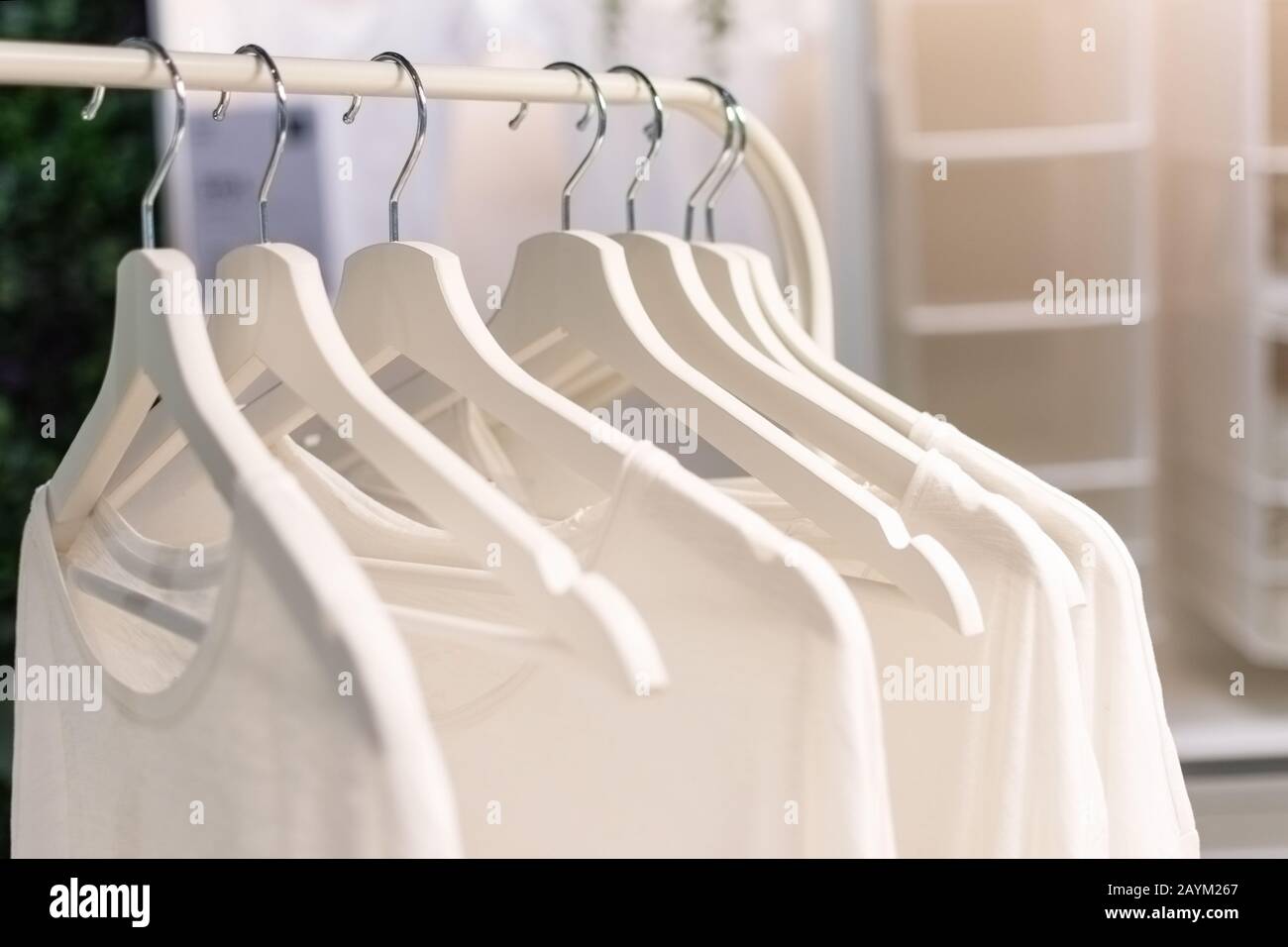 Row of white T-shirts hang on white hangers on a rack. Modern wardrobe. Stock Photo