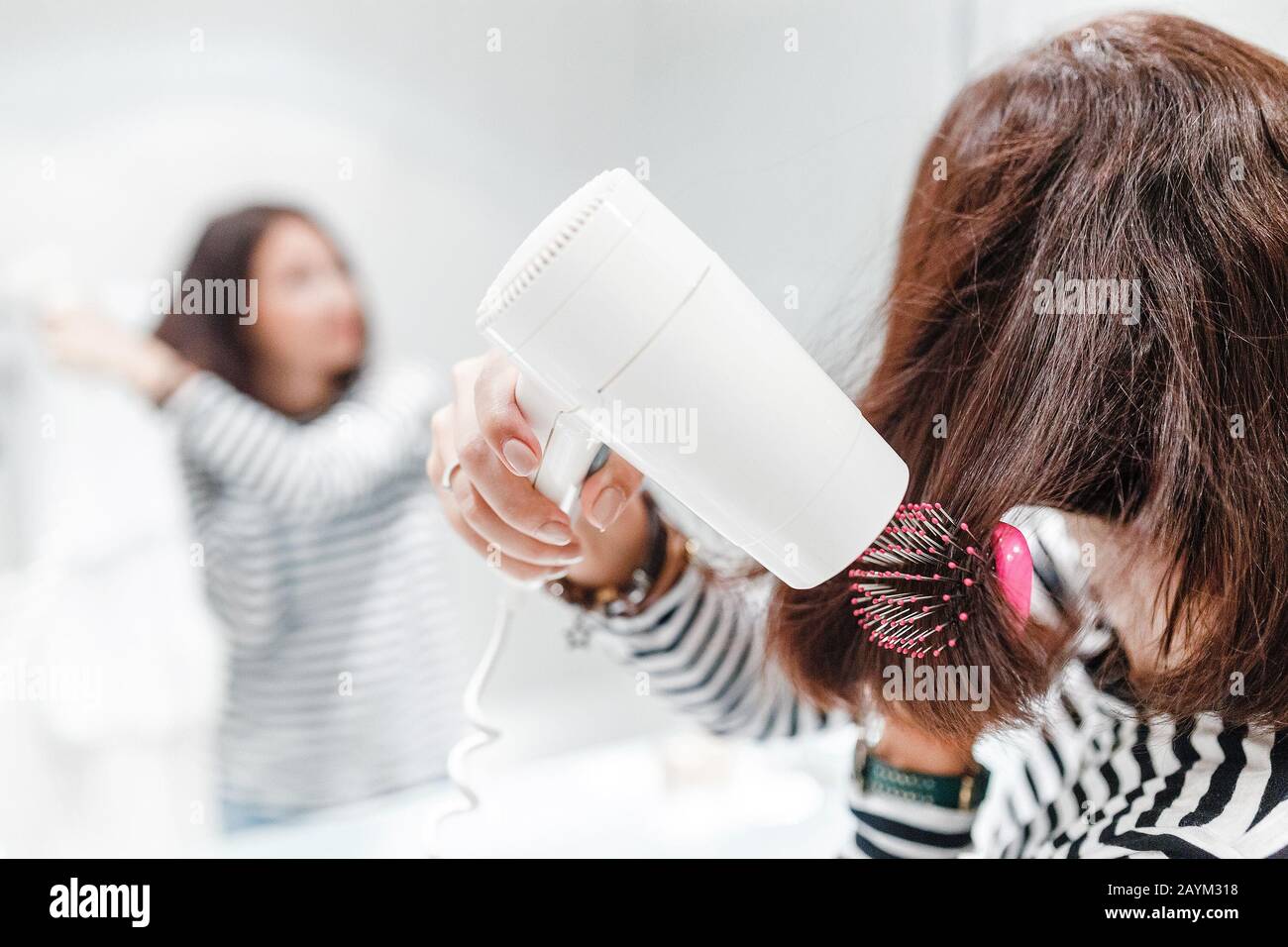 Young happy woman smiling and drying her hair with hairdryer near the mirror in the bathroom Stock Photo