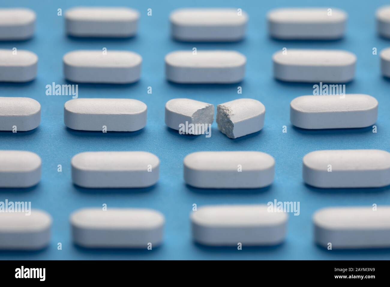 Row of White pills on blue background. One tablet is broken in half