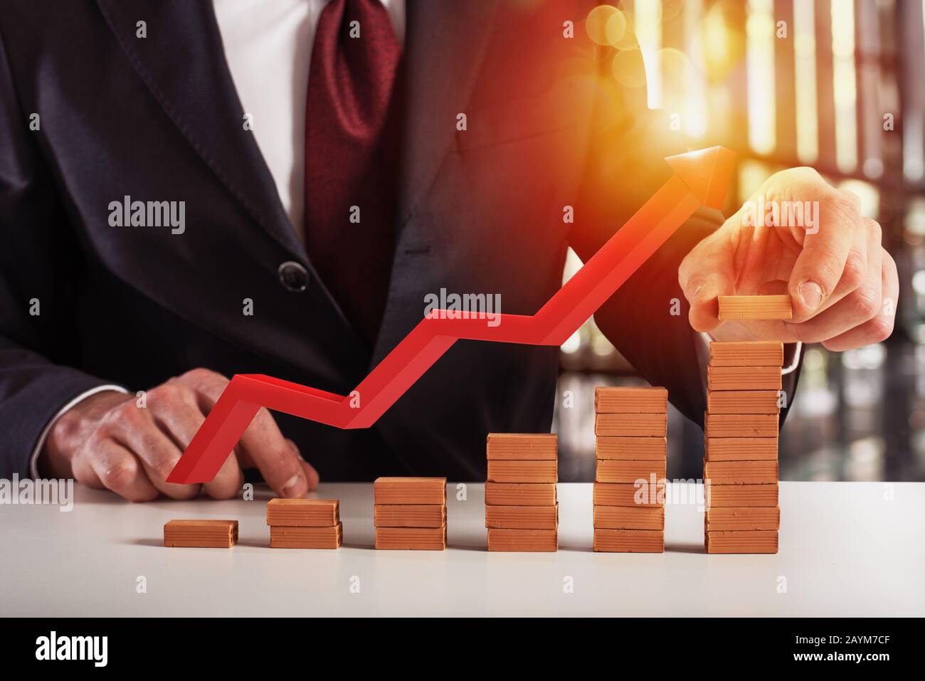 Businessman adds a brick to grow financial trend. Red arrow shows the growth. Concept of success, statistic and profit Stock Photo
