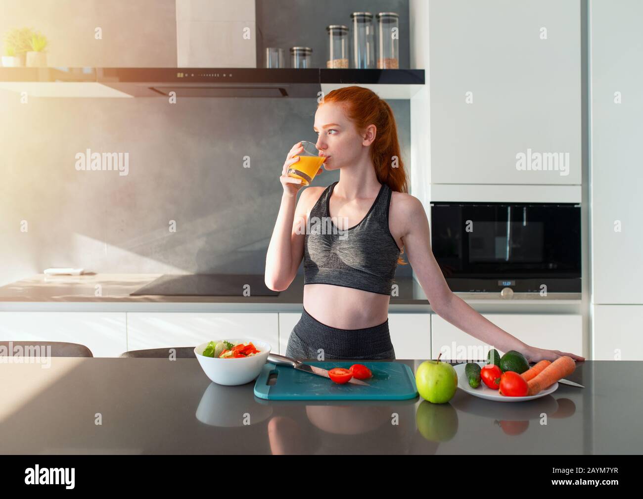 Athletic girl with gym clothes eats fruit in the kitchen Stock Photo