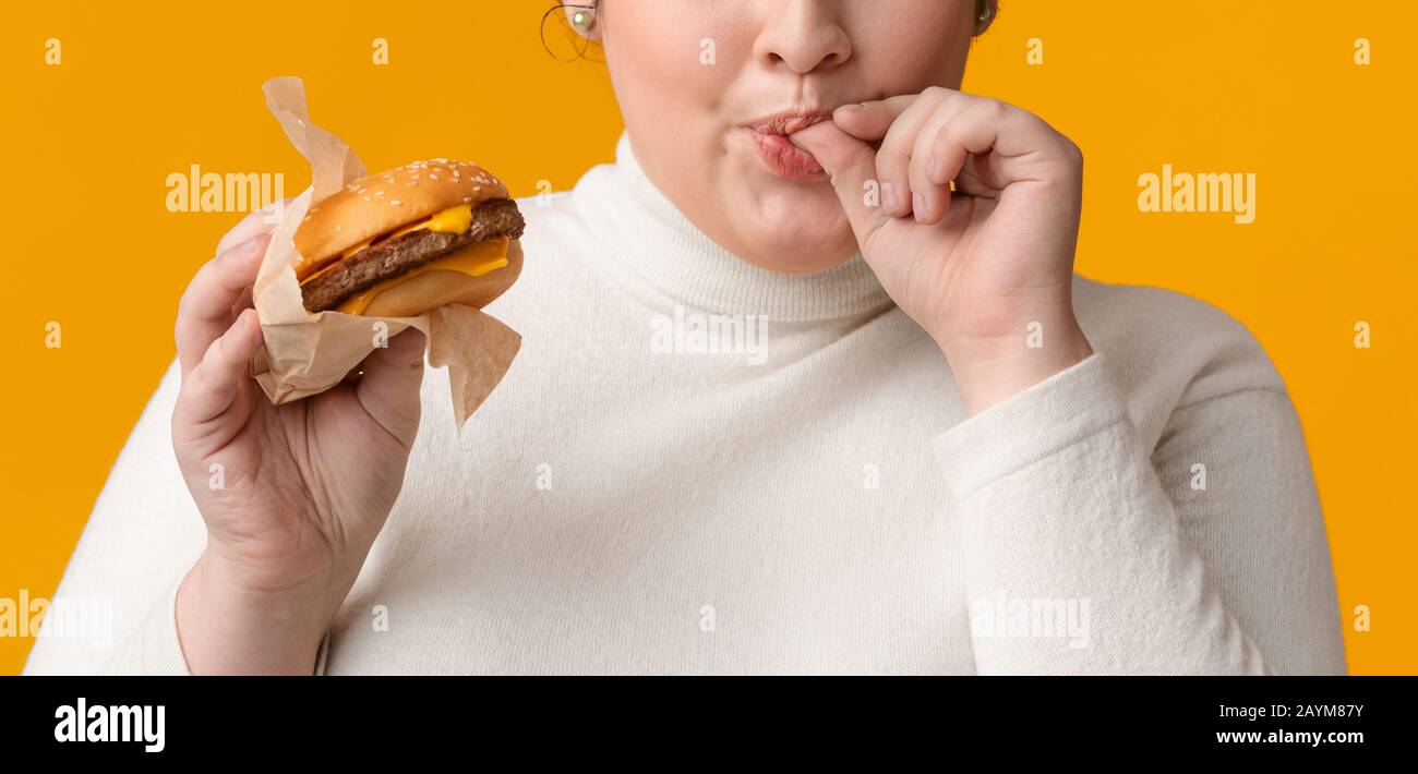 Unrecognizable Fat Girl Holding Burger And Licking Fingers With Pleasure Stock Photo