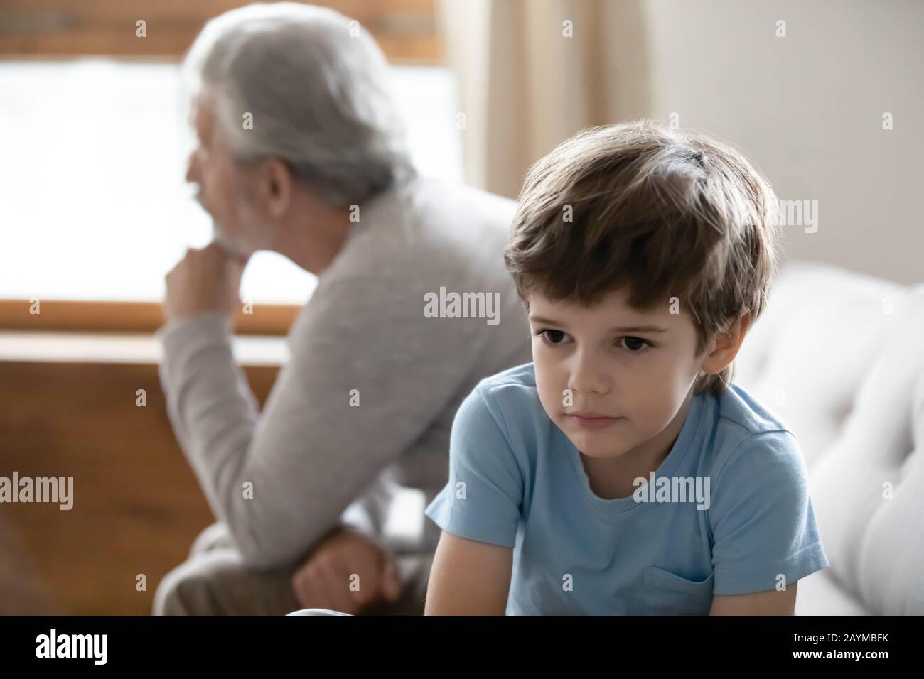 Stressed boy sitting back to back with older senior grandfather. Stock Photo