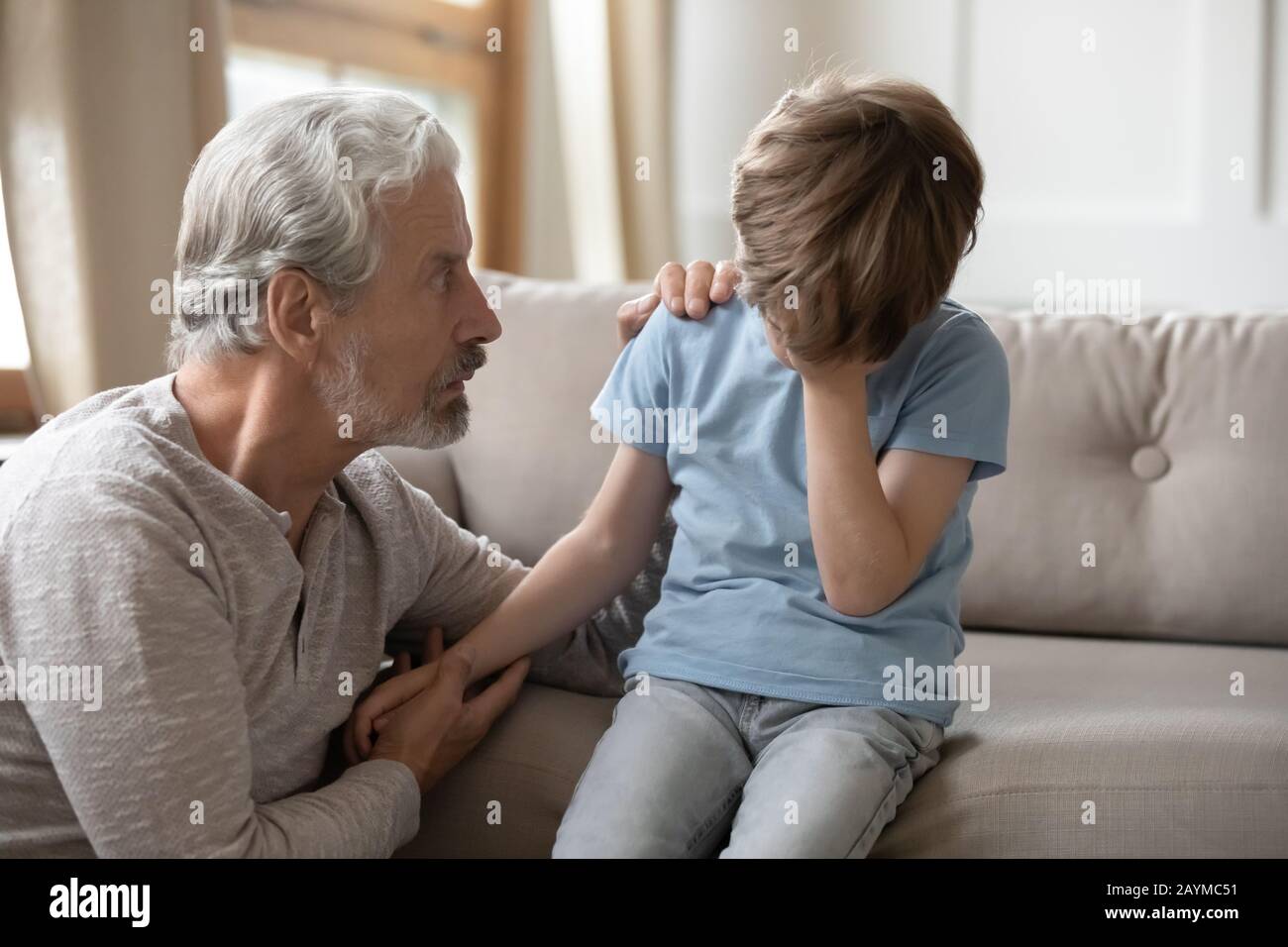 Worried middle aged hoary man supporting little offended grandchild. Stock Photo