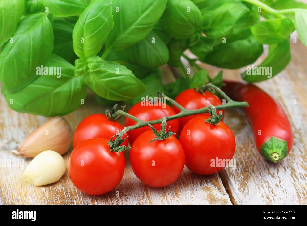 Ingredients for perfect pasta: ripe cherry tomatoes, garlic cloves and fresh basil leaves and chilli on rustic wooden surface Stock Photo