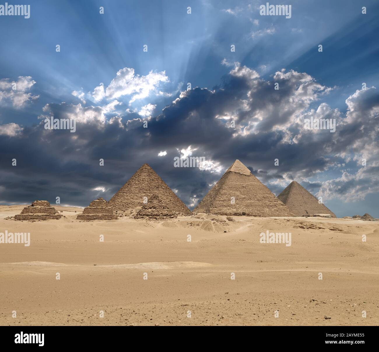 Sun shines from clouds above the Giza pyramid complex or the Giza Necropolis on the Giza Plateau in Egypt near Cairo includes the Great Pyramid of Giz Stock Photo