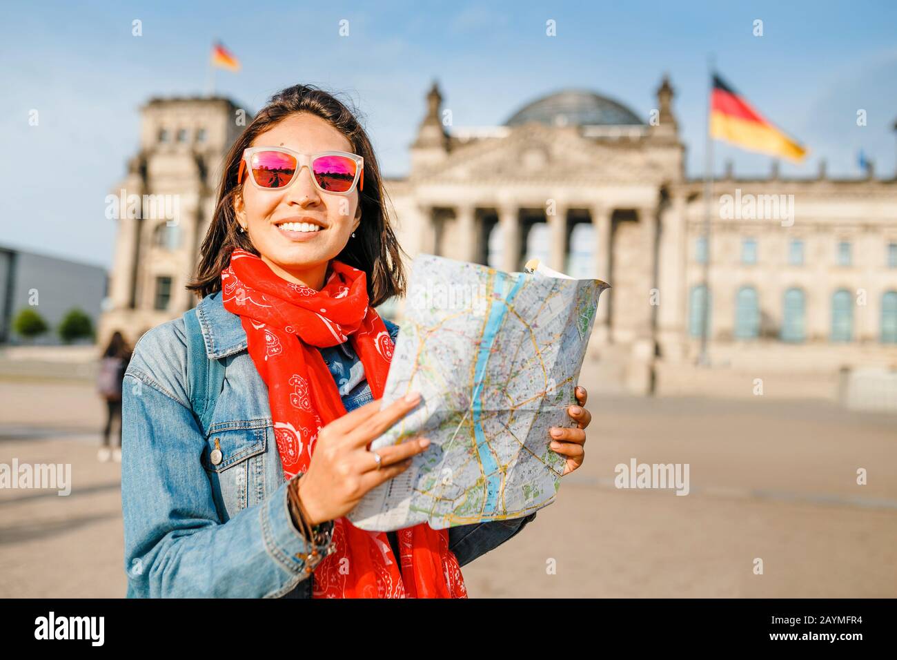 Beautiful young woman looking at map guide while standing in front of Bundestag building at sunset in Berlin. Travel in Germany concept Stock Photo