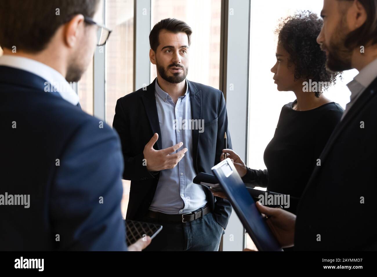 Confident businessman in suit standing telling diverse employees about project. Stock Photo