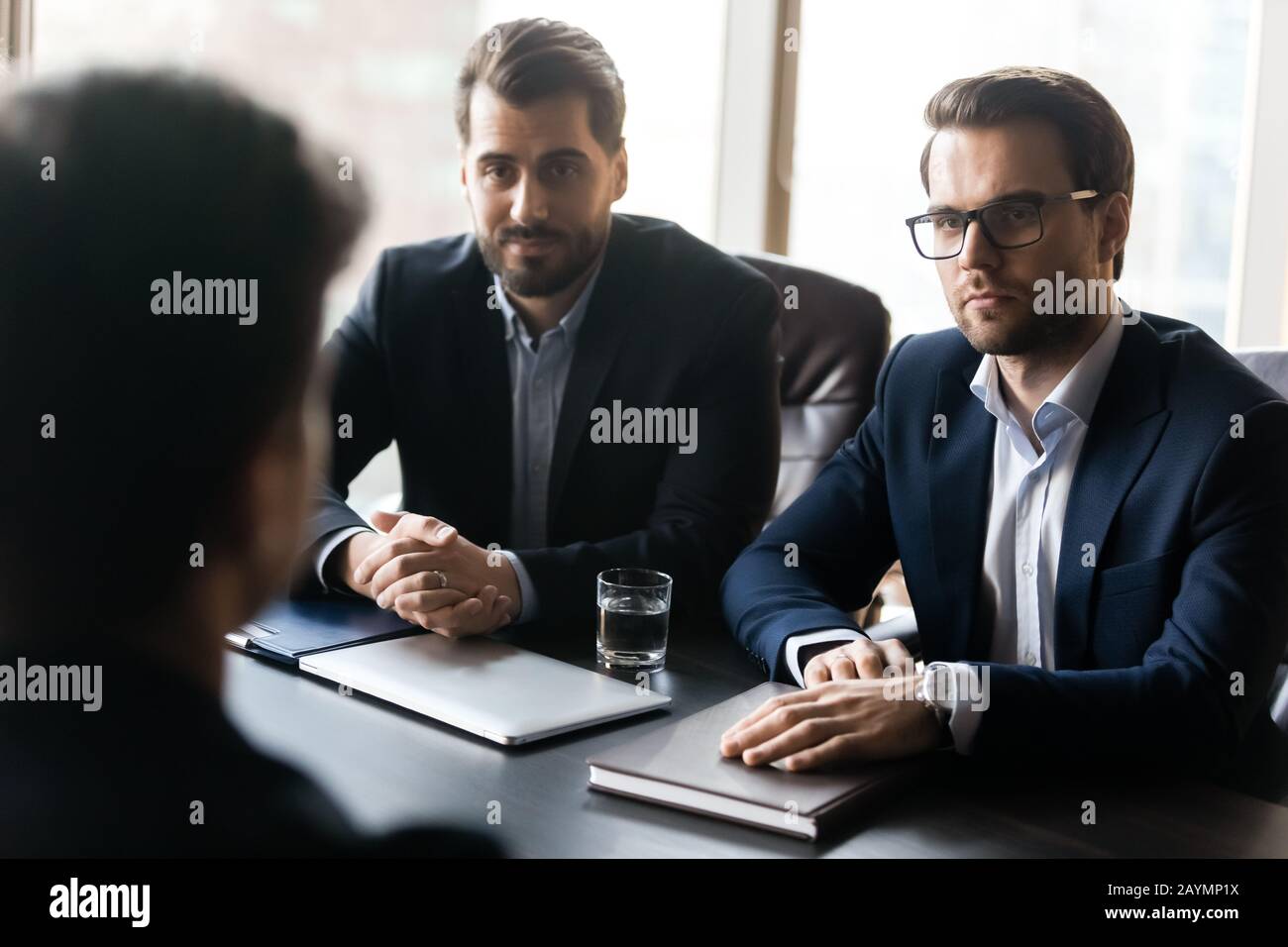 Two serious HR businessmen listening male applicant during work interview. Stock Photo