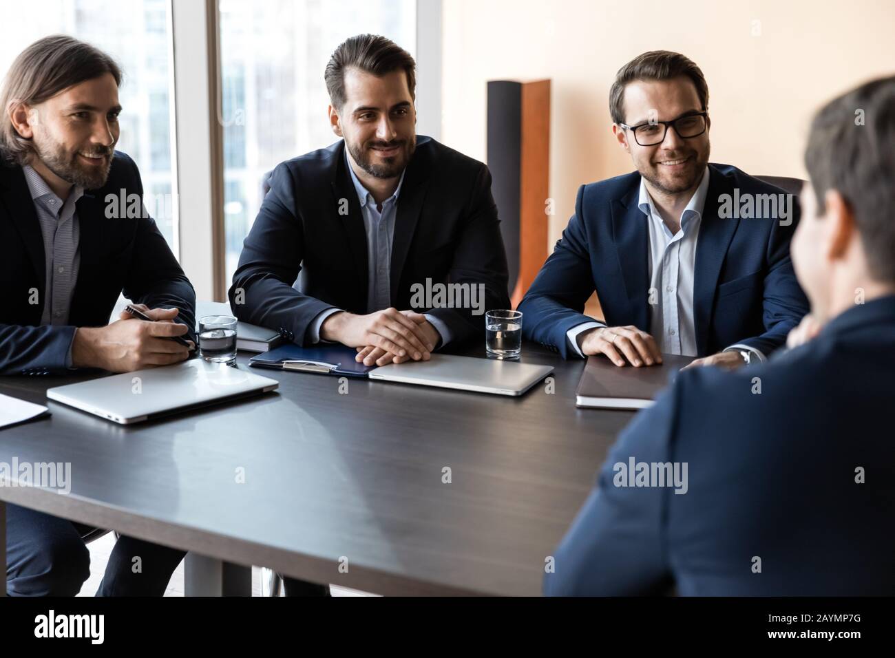 Applicant sitting in front three happy HR businessmen speaking. Stock Photo