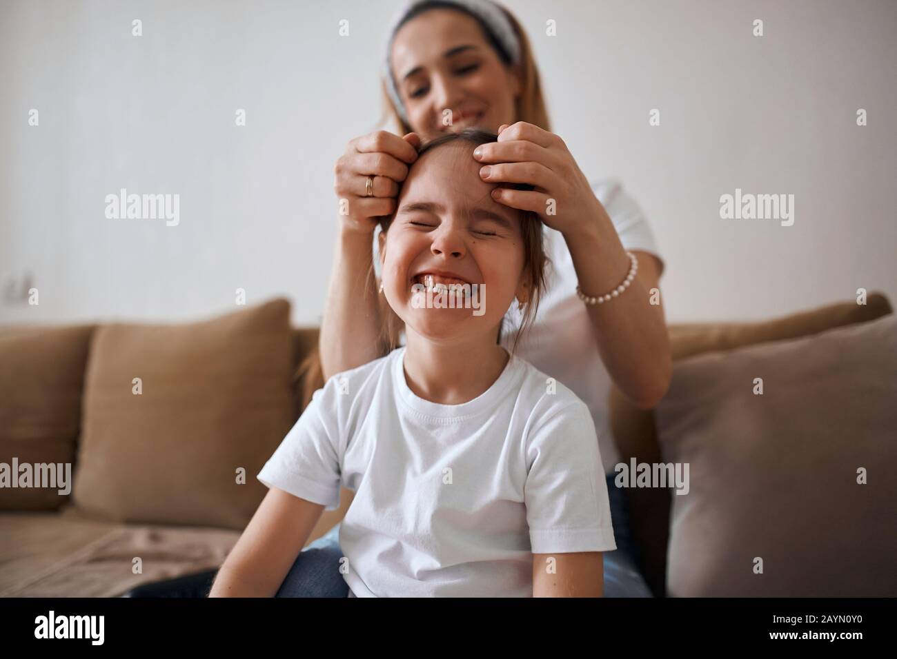 mother plaiting one braid for her child, woman doing kid's hgair, woman tightening kid's hair after the night. close up photo, funny girl making faces Stock Photo