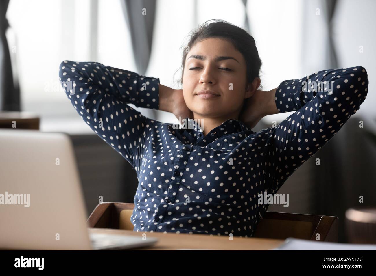 Tired ethnic woman relax in chair at workplace Stock Photo