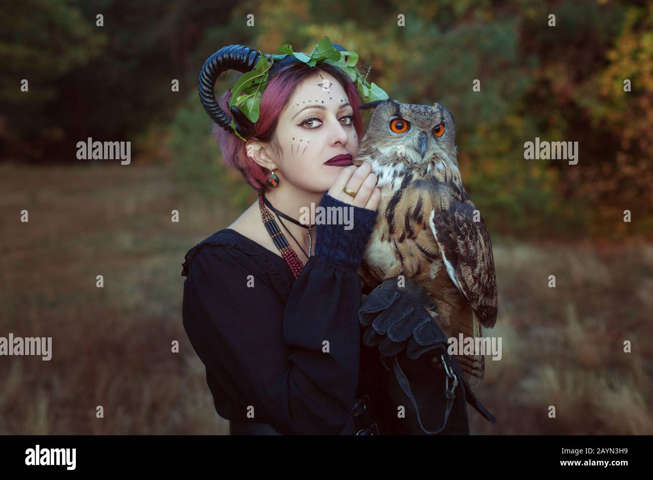 Woman shaman with horns holds an owl in her hands. Stock Photo