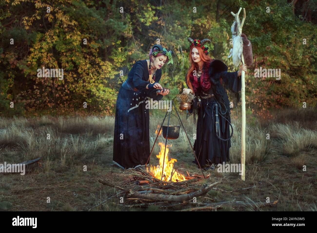 Two women shamans make a potion on a bonfire in the forest. Stock Photo