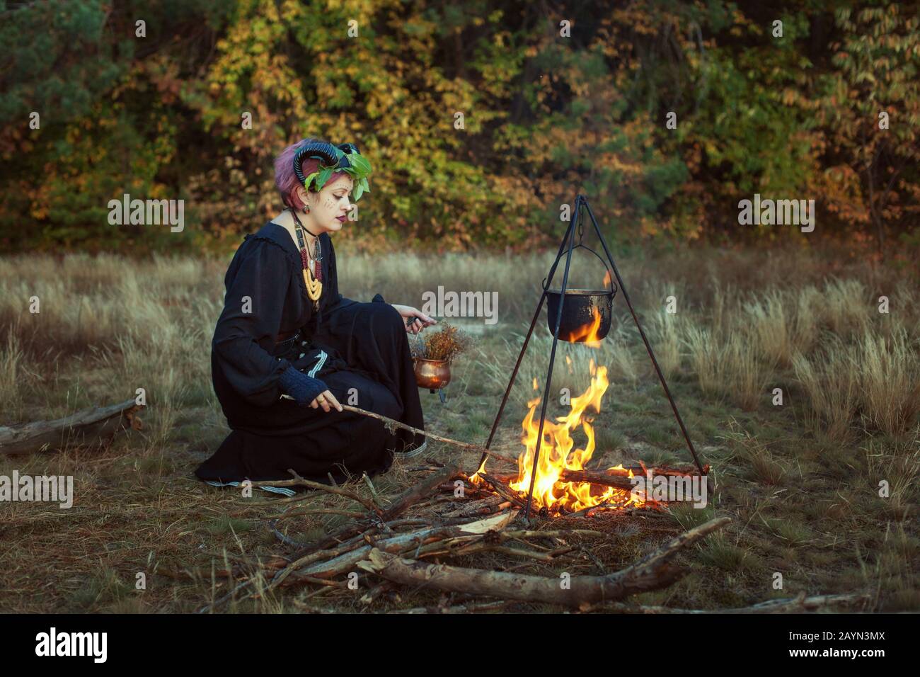 Female shaman prepares a magic potion in a forest on fire. Stock Photo