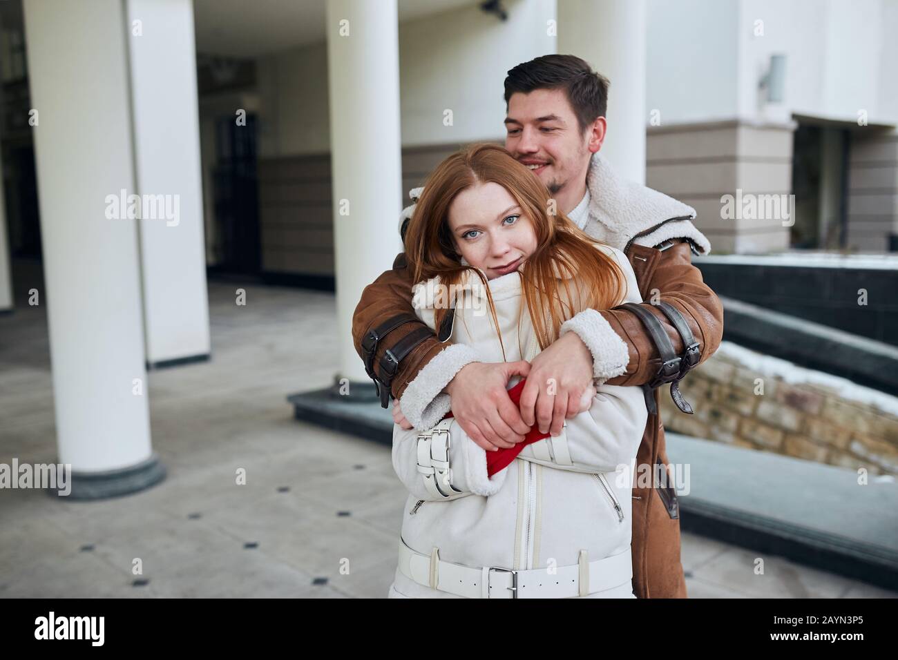 Two attractive cheerful young people hugging in the street. man standing behind her girlfriend, trying to get her warm. love, positive feeling and emo Stock Photo