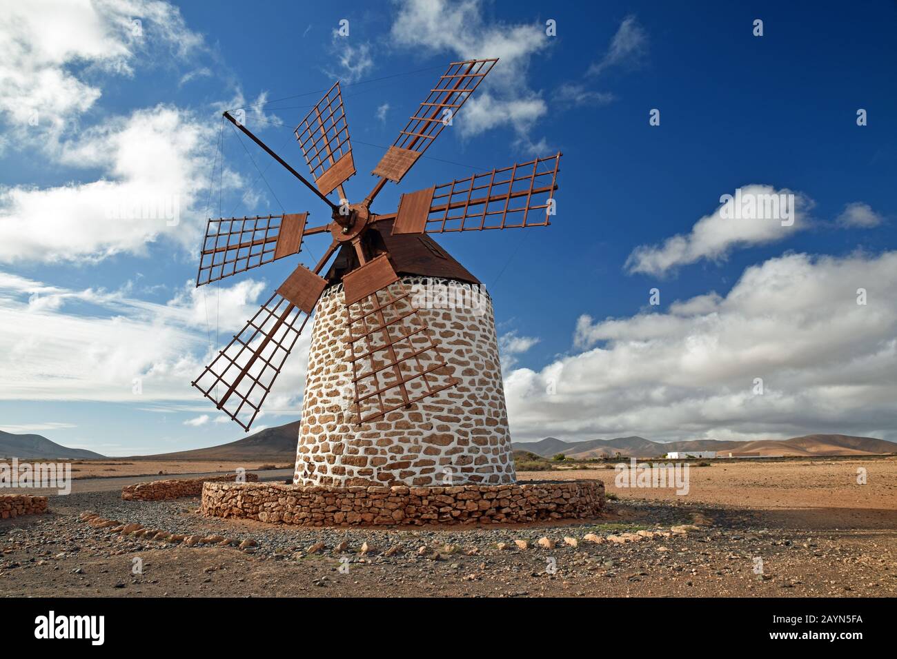 Traditional windmill at Tefia, Fuerteventura. Wooden sails and roof, round stone whitewashed building. Blue sky and clouds. Volcanic landscape. Stock Photo
