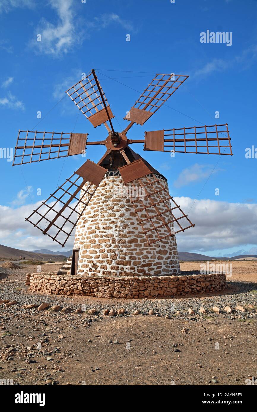 Traditional windmill at Tefia, Fuerteventura. Wooden sails and roof, round stone whitewashed building. Blue sky and clouds. Volcanic landscape. Stock Photo