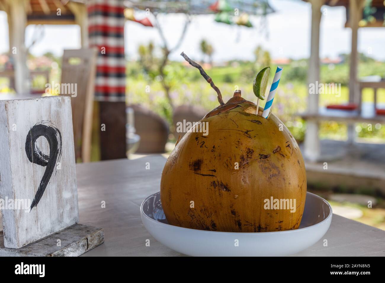Fresh coconut with paper straw and lime in an outdoor cafe. Wooden