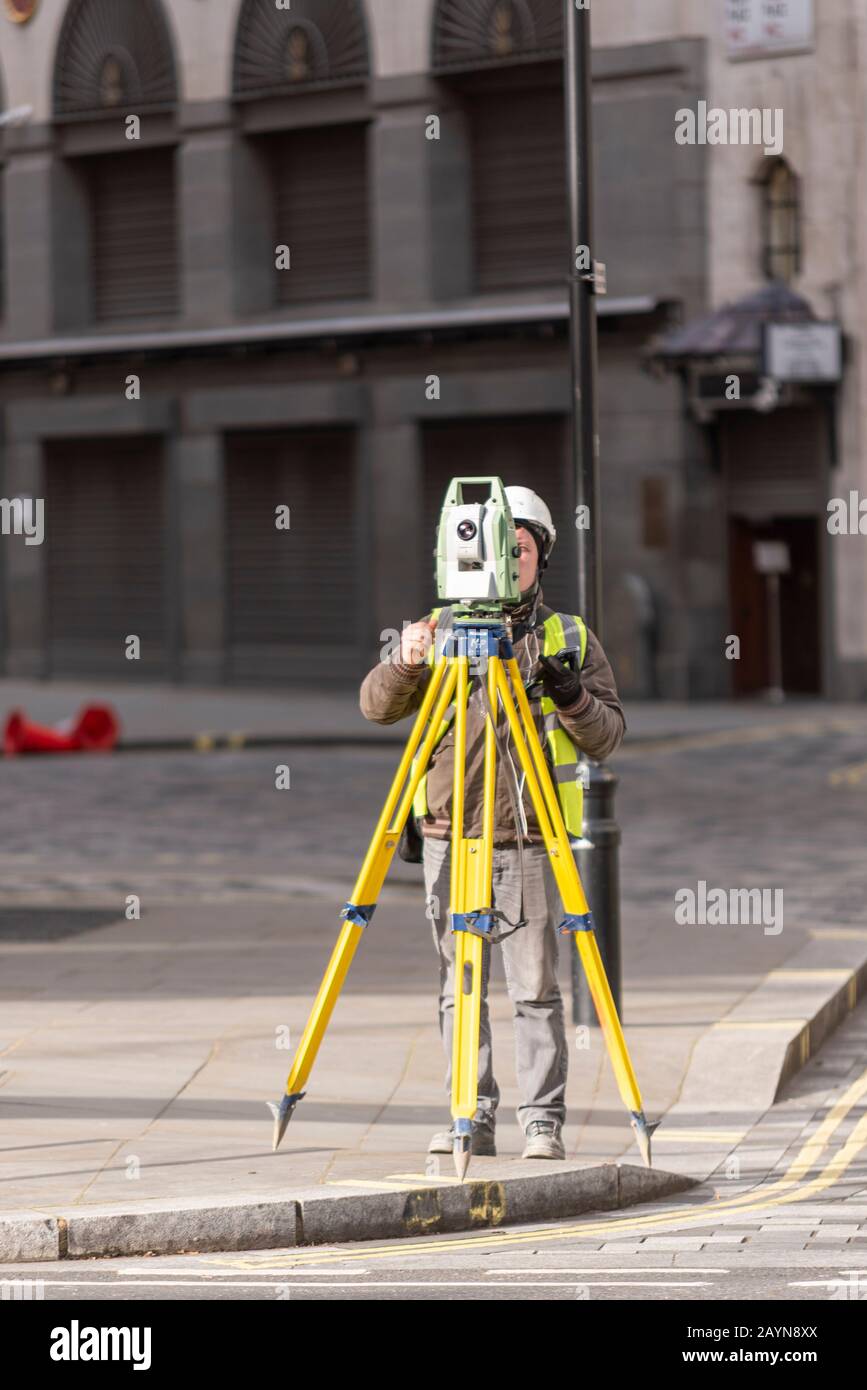 Male worker using a theodolite on a tripod to survey a location in the Strand, London, UK. Surveying in the street Stock Photo